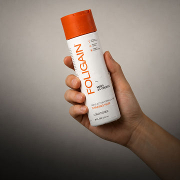 มือกำลังถือครีมนวดผมทริปเปิลแอ็กชัน FOLIGAIN สำหรับผู้ชายที่มี TRIOXIDIL 2%.