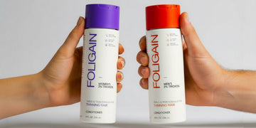 มือกำลังถือครีมนวดผม TRIOXIDIL FOLIGAIN สำหรับผู้หญิงและผู้ชายที่มีฝาสีม่วงและสีส้ม.
