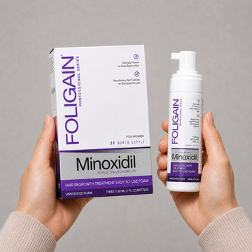 มือกำลังถือกล่องและขวดโฟมไมน็อกซิดิล 5% FOLIGAIN ชนิดทาสำหรับผู้หญิง.