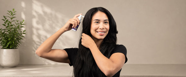 ผู้หญิงแสกผมและถือหัวพ่นสเปรย์ FOLIGAIN TRIOXIDIL ใกล้หนังศีรษะ.