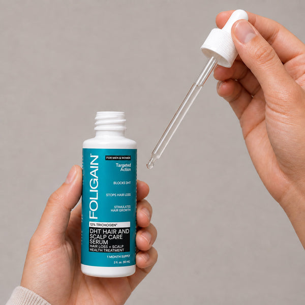 มือกำลังถือขวดเซรั่มดูแลเส้นผมและหนังศีรษะ DHT FOLIGAIN ที่เปิดฝา และหลอดหยดที่มีเซรั่มอยู่ภายใน.