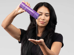 ผู้หญิงเทผลิตภัณฑ์ดูแลเส้นผมชนิดน้ำ FOLIGAIN จากขวดสีม่วงลงบนมือ